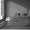 A dark gray satin duvet cover and pillowcases are neatly arranged on a bed in a dimly lit room. Anteprima dell’immagine prodotto
