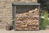 A wooden log store filled with firewood, placed against a stone wall, with an axe resting on a log in front. Produktbild-Vorschau