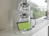 A white stand holding two white game controllers and a green handheld gaming device, with a white gaming console in the background. Produktbild-Vorschau