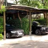 Two cars parked under a carport with lush green foliage surrounding them. Produktbild-Vorschau