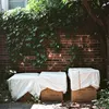 Three large cardboard boxes covered with white tarps are placed in front of a brick wall covered with ivy. Produktbild-Vorschau