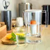 A water filter pitcher and a glass of water with lemon and mint on a kitchen counter. Produktbild-Vorschau