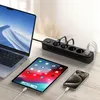 A black power strip with multiple outlets and USB ports is shown on a desk, connected to a laptop, tablet, and smartphone, all of which are charging. Anteprima dell’immagine prodotto