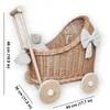 A wicker doll stroller with a teddy bear and a white bow, with dimensions indicated by text overlays. Produktbild-Vorschau