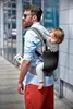 A man is carrying a baby in a carrier on his back while walking outdoors. Náhled obrázku produktu