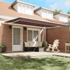 A patio scene with a retractable awning extended over a deck, featuring outdoor furniture and landscaping. Produktbild-Vorschau