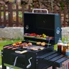 A charcoal grill with food cooking on it, set up outdoors in a garden. Anteprima dell’immagine prodotto