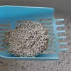 A close-up of a blue litter scoop filled with white clumping cat litter, some of which is mixed with small blue particles. Anteprima dell’immagine prodotto
