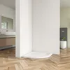 A modern bathroom with a white corner shower tray on a wooden floor, a toilet and a vanity with a mirror in the background. Produktbild-Vorschau
