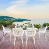 A dining set with white chairs and a table is placed on a wooden deck overlooking a scenic beach and ocean view. Náhled obrázku produktu