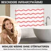 A woman enjoying the warmth of an infrared heater in a bathroom setting. Produktbild-Vorschau
