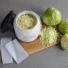 A food storage container with shredded cabbage, whole cabbages, and a cutting tool on a wooden board. Produktbild-Vorschau