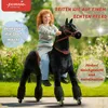 A young girl with red hair rides a black mechanical horse in an outdoor setting with greenery and sunlight. Anteprima dell’immagine prodotto