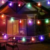 A string of colorful LED lights illuminates a patio area at dusk, with a house and outdoor furniture visible. Produktbild-Vorschau