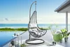 An outdoor hanging chair with cushions is placed on a deck next to a pool with the ocean in the background. Produktbild-Vorschau