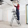A person is standing on a step ladder, working on a ceiling light fixture in an unfinished room. Anteprima dell’immagine prodotto