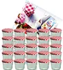 A collection of small glass jars with red and white checkered lids, arranged in rows, with some decorative elements like flowers and a packet of gelling agent in the background. Produktbild-Vorschau