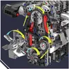 A close-up view of a complex mechanical assembly, likely a model engine, with various gears, chains, and moving parts indicated by arrows. Náhľad obrázku produktu