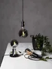 Three decorative LED light bulbs are displayed on a white surface against a gray background. One bulb hangs from a black cord, another sits on a black base, and the third lies on its side. Podgląd zdjęcia produktu