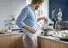 A man is using a sous vide cooker in a modern kitchen, with other people in the background. Produktbild-Vorschau