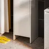 A close-up view of a white cabinet with a textured door, next to a black tiled wall. Yellow flip-flops are on the floor in the foreground. Produktbild-Vorschau