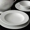 A close-up view of white porcelain dinnerware with ornate embossed patterns. Produktbild-Vorschau