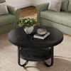 A round black coffee table with a two-tier shelf is placed in a living room setting with green sofas and chairs. Produktbild-Vorschau