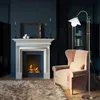 A cozy living room scene with a fireplace, armchair, and floor lamp. Produktbild-Vorschau