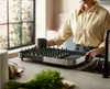 A person is placing a dish rack on a kitchen counter next to a sink. Voir les images du produit
