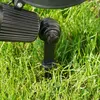 A close-up view of a black outdoor spotlight stake inserted into green grass. Produktbild-Vorschau