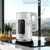A white electric kettle with an LED display is shown on a kitchen counter, with a window in the background showing a landscape. Náhled obrázku produktu