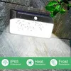 A solar-powered wall light is mounted on a stone wall during a rain shower. The light is illuminated and casts a bright glow downwards. There are icons at the bottom indicating waterproof, heat resistance, and frost resistance. Náhled obrázku produktu