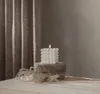 A white bubble candle with a warm white LED light is placed on two stones, with dried grass in the foreground and a textured curtain in the background. Podgląd zdjęcia produktu