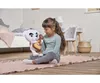 A young girl is sitting on a rug in a bedroom, holding a plush toy dog with a guitar. Produktbild-Vorschau