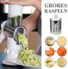 Weiße und silberne Drehreibe in Gebrauch, schreddert Zucchini auf einen weißen Teller, mit Beispielen für geschredderten Käse, Karotten und Kartoffeln Voir les images du produit