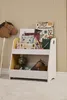 A children's bookshelf filled with books and toys, set against a striped wallpaper. Produktbild-Vorschau