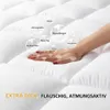 Weiße gesteppte Matratzenauflage mit einer Hand, die darauf drückt, zeigt Weichheit und Flauschigkeit, mit Feature-Blasen Náhľad obrázku produktu