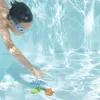 A child is underwater in a swimming pool, reaching for colorful toy fish on the pool floor. Anteprima dell’immagine prodotto