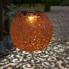 A decorative solar lantern ball sits on a gravel path in a garden at dusk, casting patterned light. Produktbild-Vorschau