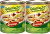 Two cans of Erasco Chinesischer Gemüsetopf (Chinese Vegetable Stew) are shown side-by-side against a background that transitions from yellow at the top to green at the bottom, with a subtle illustration of fields and houses. Náhled obrázku produktu