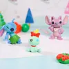 A collection of small figurines, including Stitch, Angel, and Scrump, arranged on a light-colored surface with decorative elements in the background. Produktbild-Vorschau