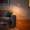 A floor lamp illuminates a corner of a living room with a sofa and an open book. Produktbild-Vorschau