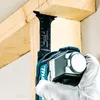 A person wearing a white glove is using a Makita cordless multi-tool to cut into a wooden beam. Produktbild-Vorschau