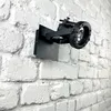 A black spotlight fixture is mounted on a white brick wall. Anteprima dell’immagine prodotto