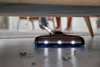 A vacuum cleaner head with lights is shown cleaning under a piece of furniture, with a person's legs visible in the background. Produktbild-Vorschau