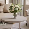 A close-up view of a modern living room setting, featuring a coffee table with a vase of white flowers and a book. Náhľad obrázku produktu