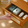 A hand is opening a drawer of a wooden nightstand, revealing items inside. Náhled obrázku produktu