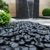 Schwarze Kieselsteine nass mit Wassertropfen vor einem Gartenbrunnen Produktbild-Vorschau