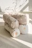 A stack of three cylindrical pillows with different patterns, placed on a textured rug with sunlight casting shadows. Produktbild-Vorschau