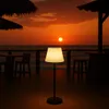 A solar-powered floor lamp is illuminated on a wooden deck at sunset, with the ocean and a bar in the background. Produktbild-Vorschau